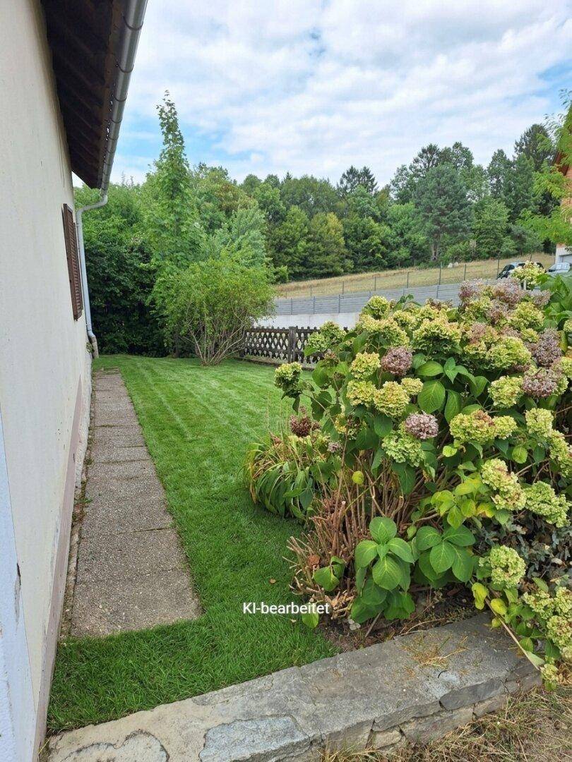 Seitlicher Gartenweg entlang des Hauses mit üppigen Hortensien und Rasenfläche.