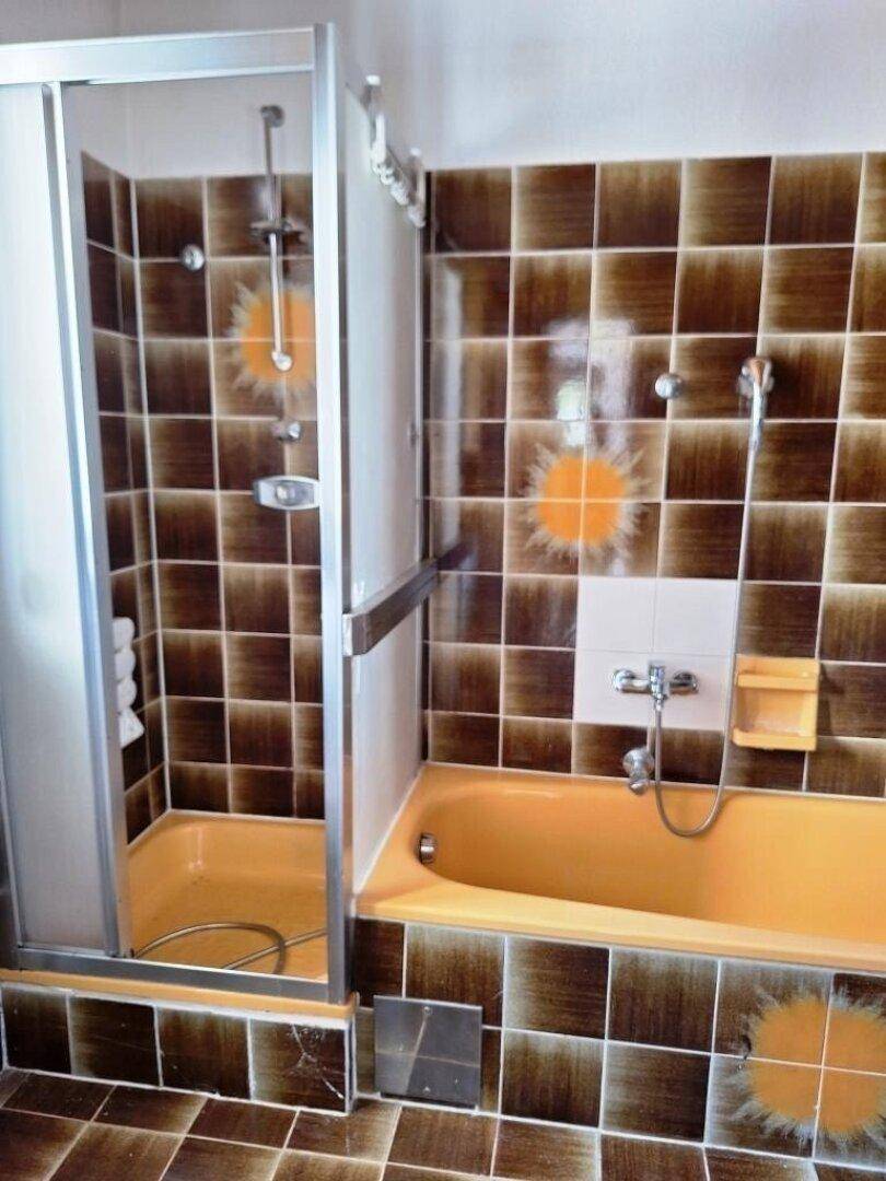 Badezimmer im Stil der 80er Jahre mit braunen Fliesen, orangefarbener Badewanne und Dusche.