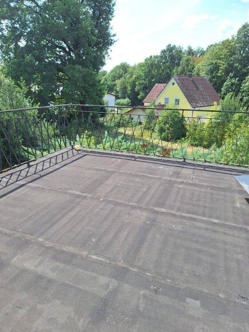 Unfertige Dachterrasse mit Metallgeländer und weitem Blick ins Grüne.