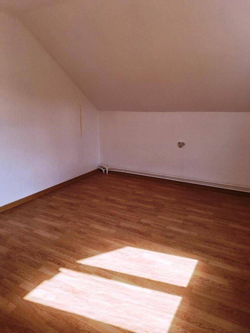 Leeres Zimmer im Dachgeschoss mit Laminatboden und sonnigen Lichtflecken.