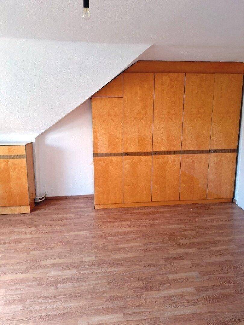 Dachgeschosszimmer mit schrägen Wänden und integrierten Holzschränken.