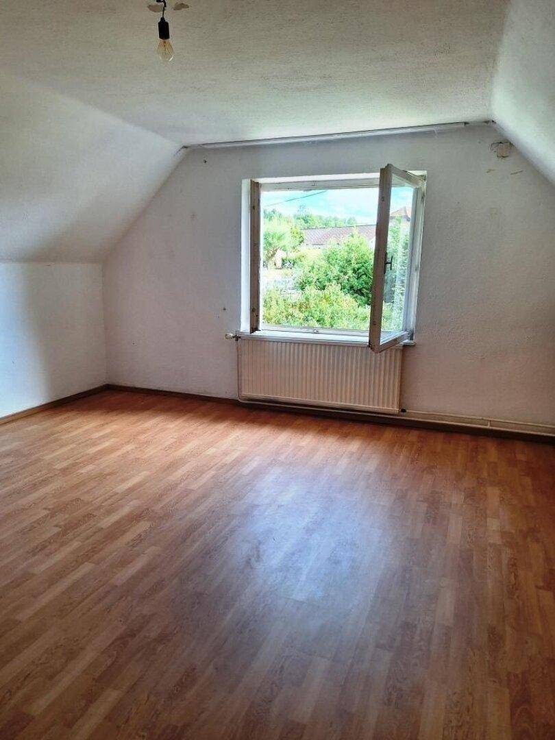 Helles Zimmer im Dachgeschoss mit Laminatboden und Ausblick ins Grüne.