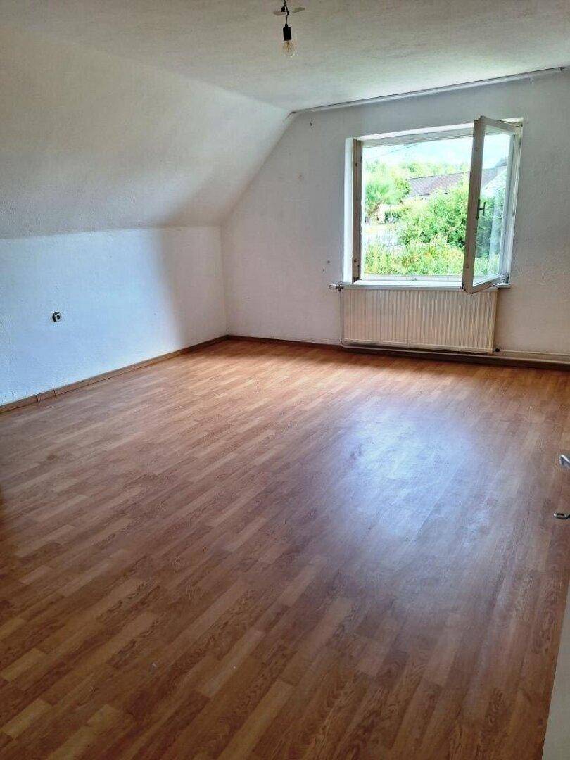 Geräumiges Dachgeschosszimmer mit Laminatboden und Fenster mit Blick auf die Umgebung.