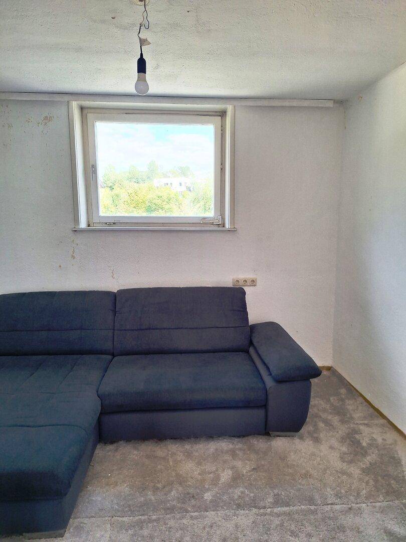 Wohnzimmer mit blauem Ecksofa und Fenster, der Boden ist noch nicht fertiggestellt.