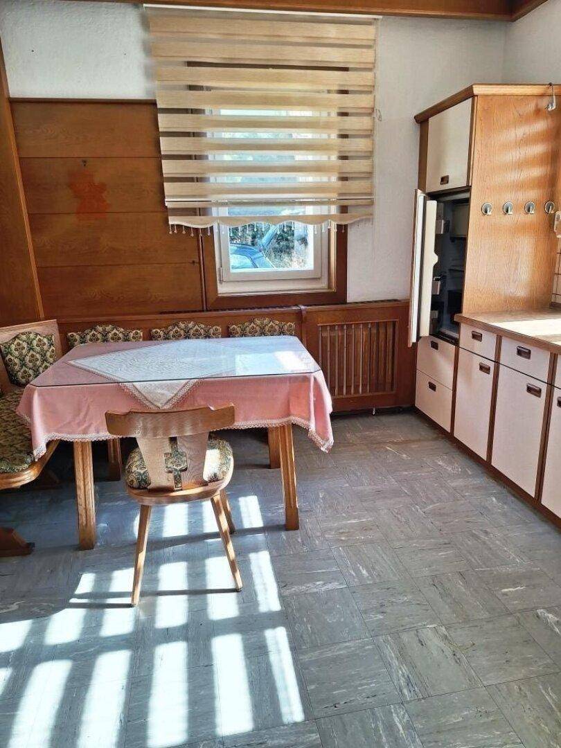Traditionelle Küche mit Holzelementen, einem Esstisch und gefliestem Boden, mit viel Tageslicht.