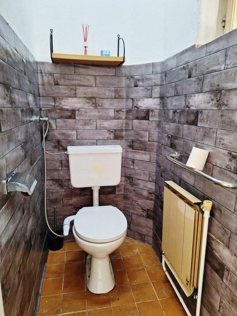 Kleines WC mit Toilette, Heizkörper und dunkler Ziegelmuster-Tapete, mit Terrakotta-Boden.
