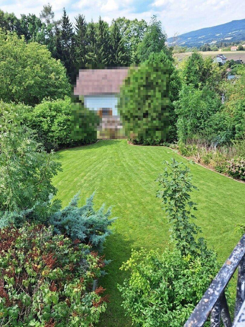 Gepflegter Garten mit Rasenfläche und Bäumen, im Hintergrund ein Haus in ländlicher Umgebung.