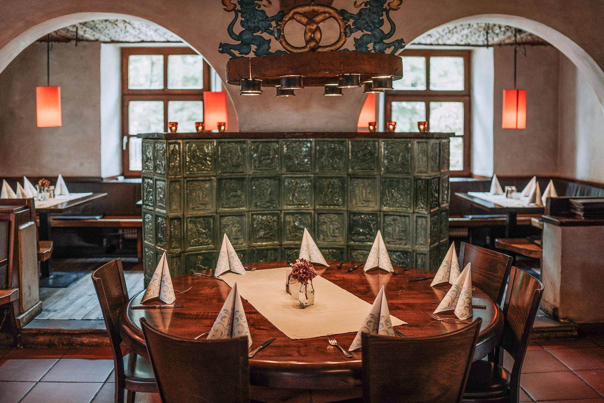 Gemütlicher Restaurantbereich mit rustikalem Holztisch, Kachelofen und traditioneller Dekoration.