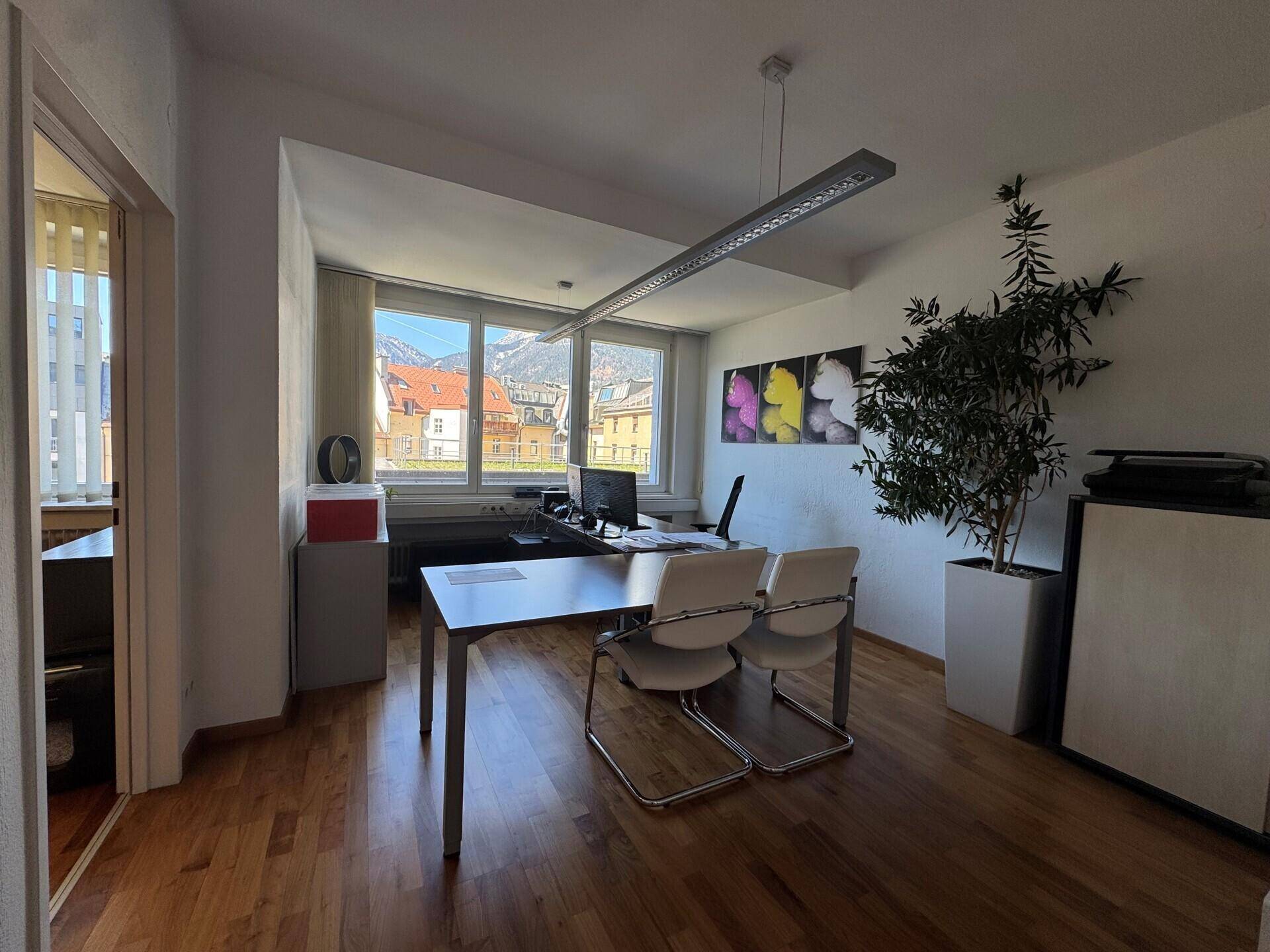 Büro mit Holzboden, Schreibtisch und Stühlen, bietet einen weiten Blick auf Berge und Gebäude.