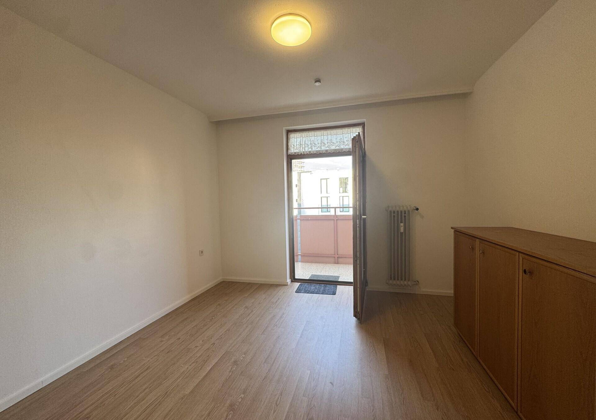 Heller Raum mit Holzboden und Zugang zu einem Balkon, bietet viel natürliches Licht.