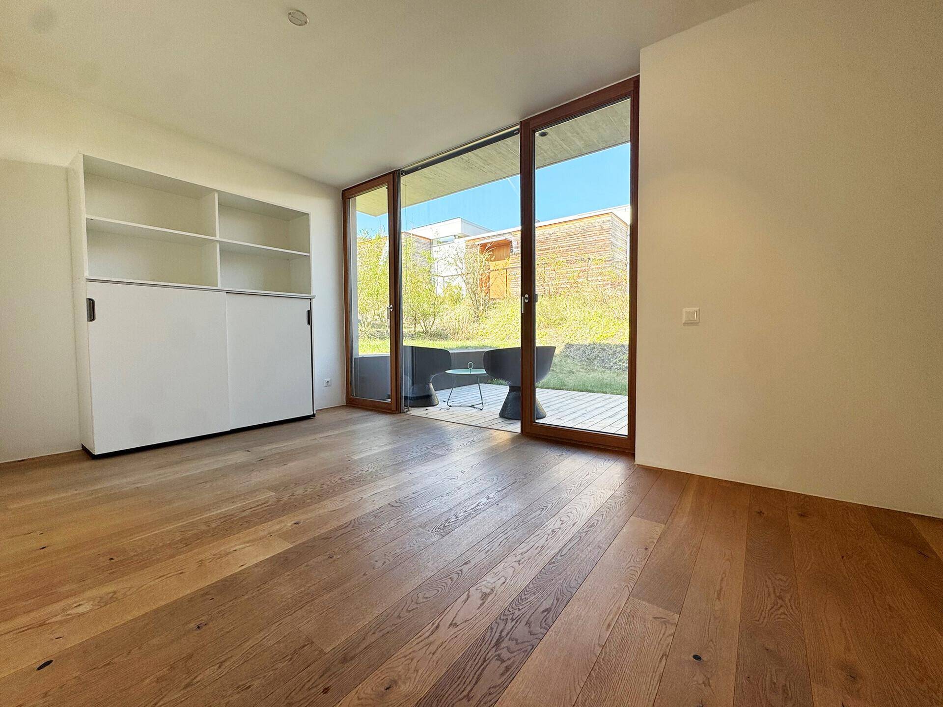 Schlafzimmer mit Holzboden, Einbauschrank und großen Schiebetüren zum Gartenbereich.