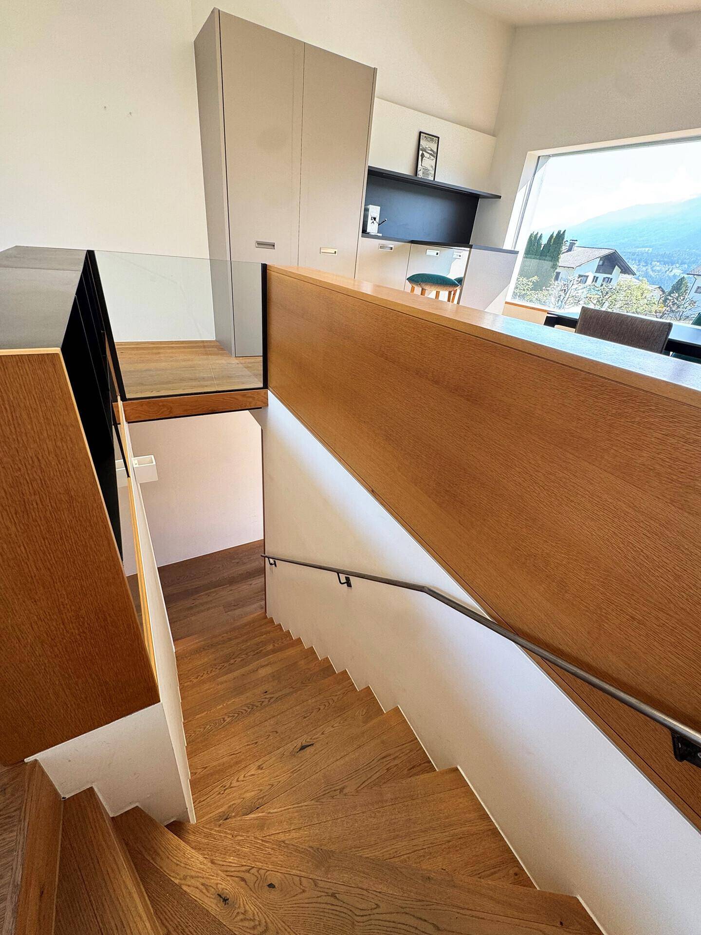 Moderne Holztreppe mit Glasgeländer, die die verschiedenen Ebenen des Hauses verbindet.