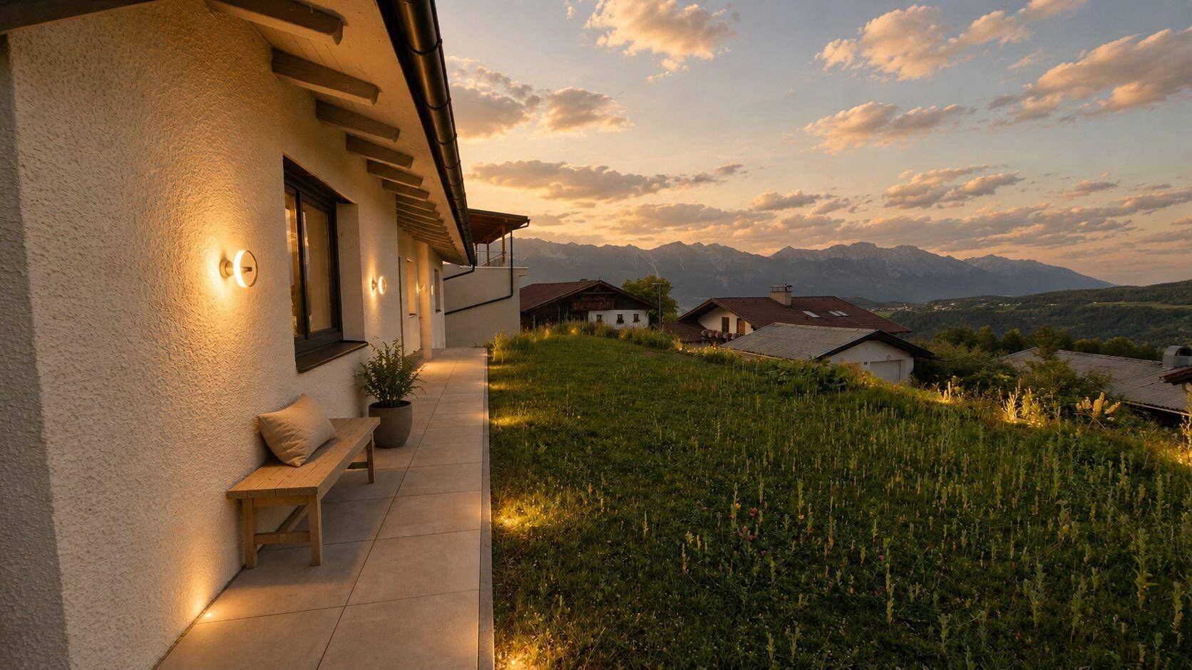 Seitlicher Zugang zum Haus mit gepflastertem Weg und Beleuchtung, umgeben von grünen Hügeln und Bergblick.