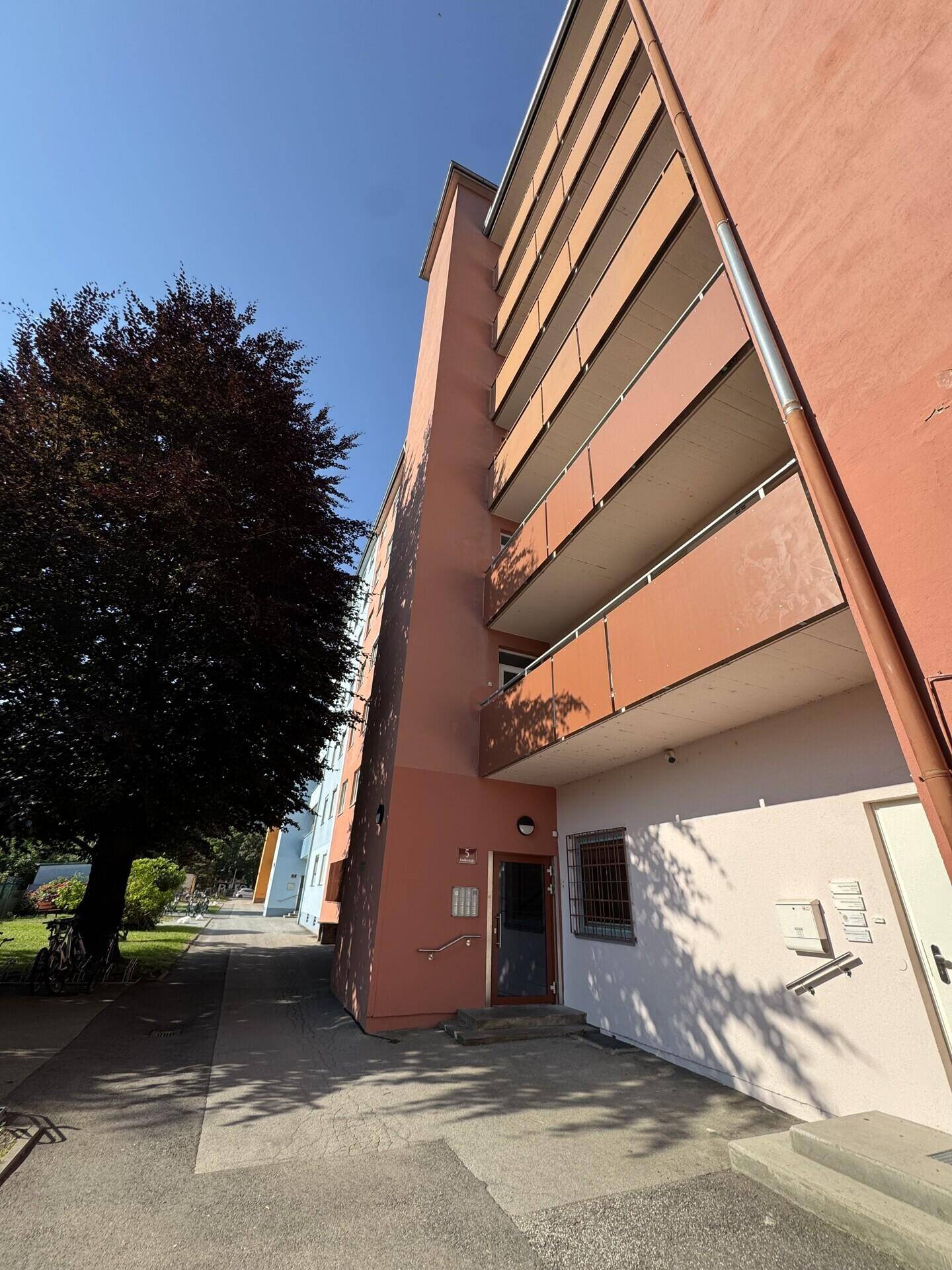 Fassade des Wohngebäudes mit Balkonen und Eingangsbereich, umgeben von Grünflächen.
