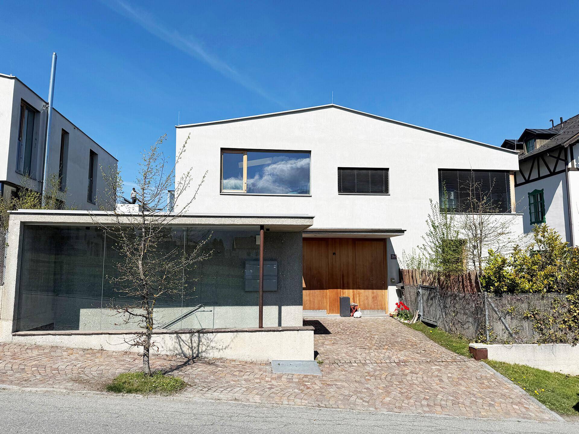 Gesamtansicht der modernen Hausfassade mit gepflasterter Auffahrt und angrenzendem Gebäude.