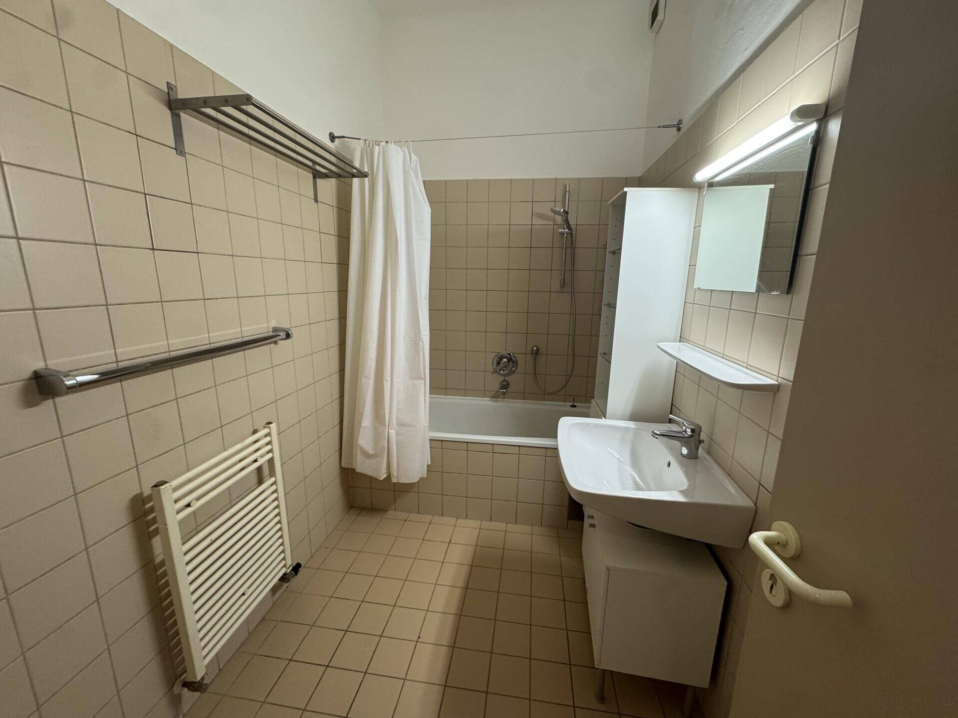 Funktionales Badezimmer mit Badewanne, Waschbecken, beigefarbenen Fliesen und Handtuchheizkörper.