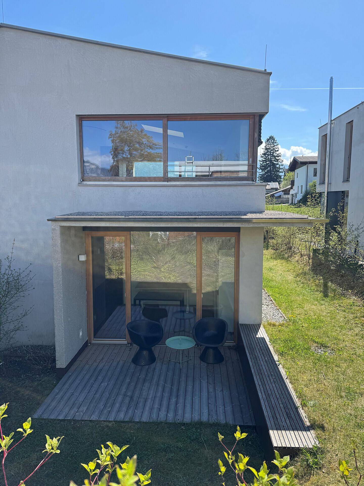 Ansicht der Holzterrasse mit Garten und der Rückseite des modernen Gebäudes.