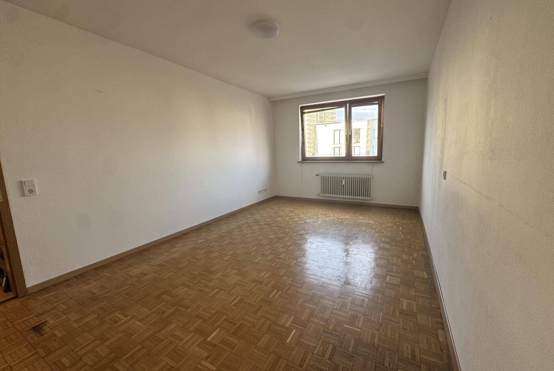 Geräumiges Zimmer mit Parkettboden und Fenster, ideal als Schlaf- oder Arbeitszimmer nutzbar.