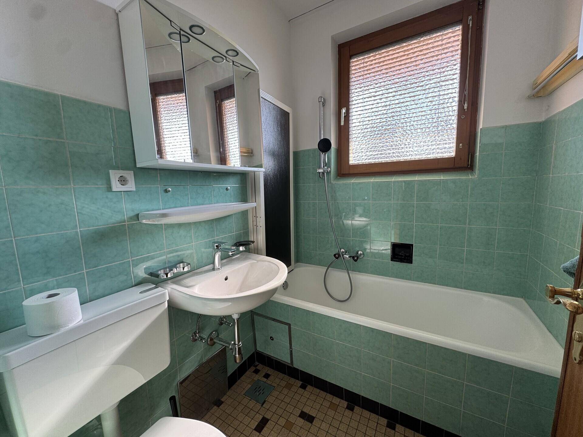 Badezimmer mit grünen Fliesen, Badewanne, Waschbecken und Spiegelschrank, funktional und hell.