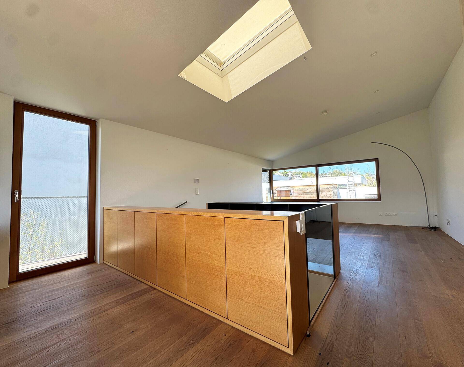 Offener Wohnbereich mit Holzboden, Einbauschrank, Dachfenster und Zugang zu einem Balkon.