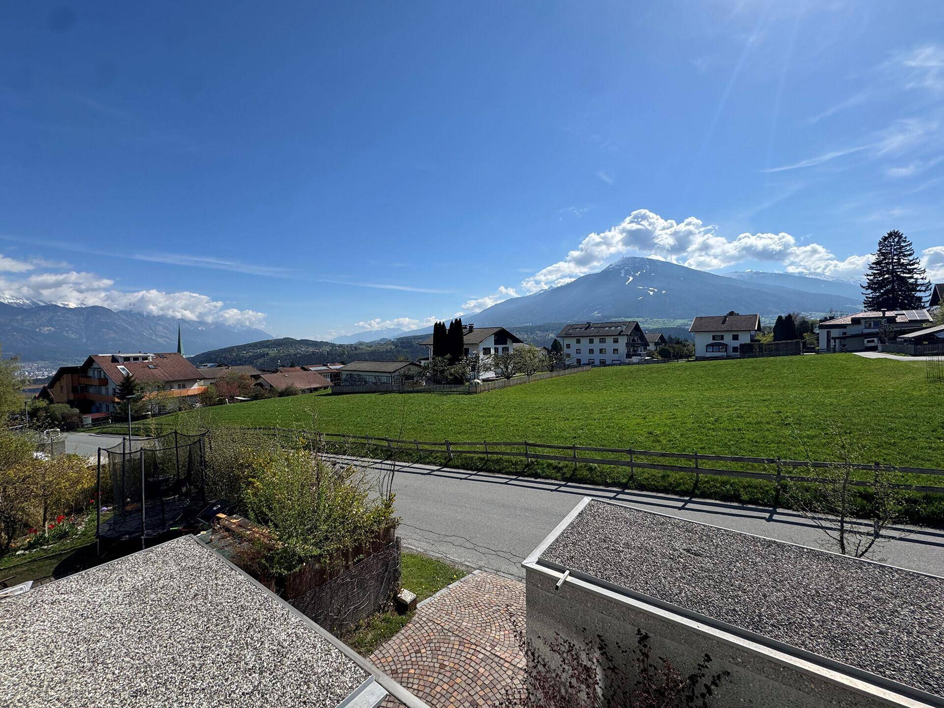 Weitläufiger Blick auf die grüne Landschaft mit Häusern und majestätischen Bergen im Hintergrund.