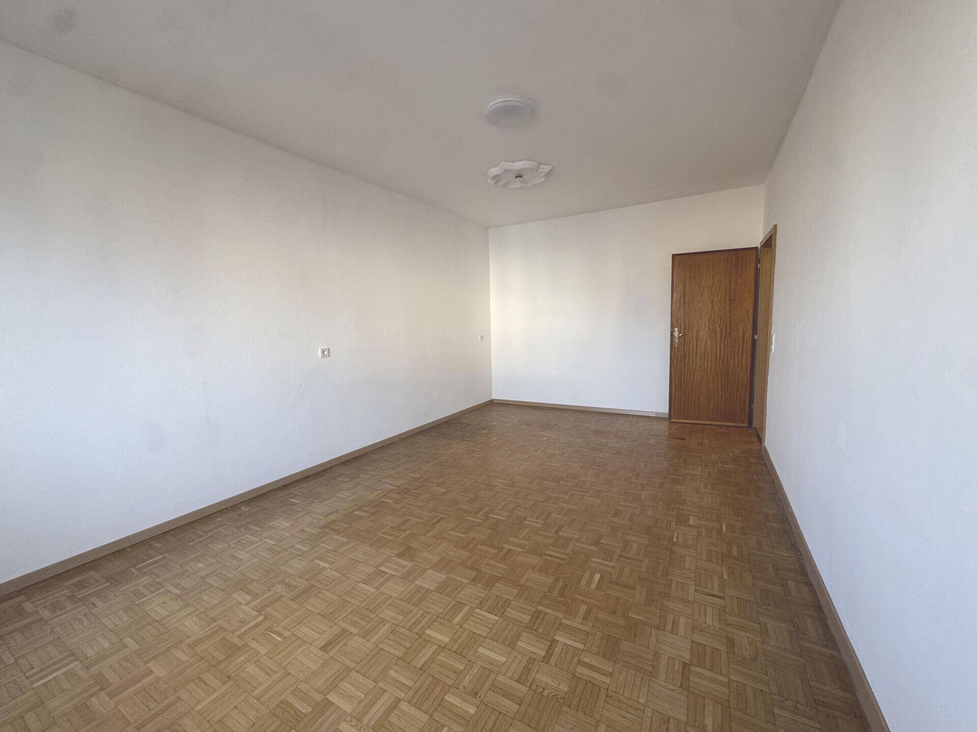 Leerer Raum mit Parkettboden und einer Holztür, bereit für individuelle Gestaltung.
