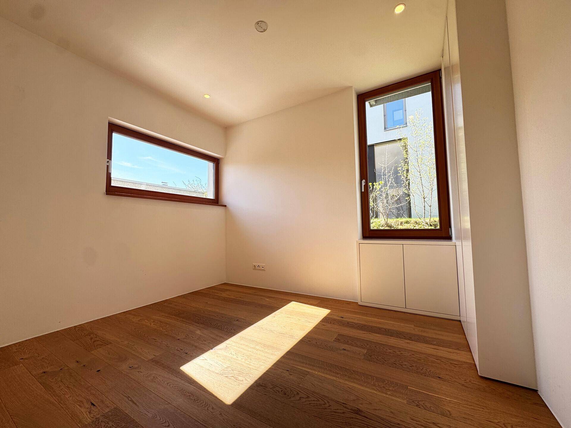 Geräumiges Schlafzimmer mit Holzboden und Fenstern, die einen Blick ins Grüne bieten.