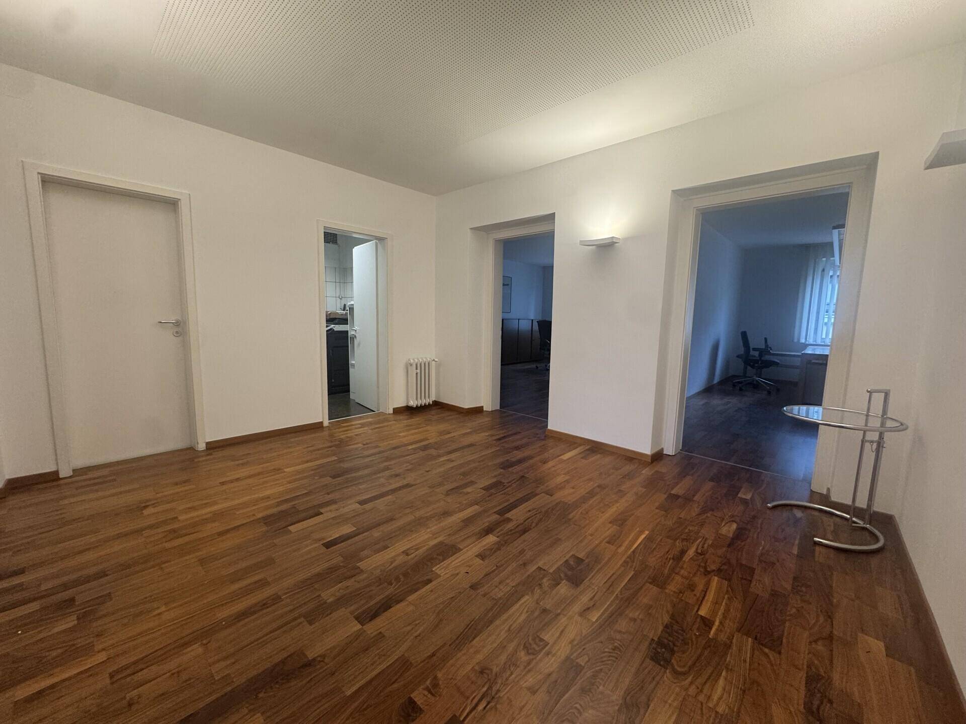Heller Flur mit Holzboden, der zu verschiedenen Räumen führt, darunter ein Büro und eine Küche.