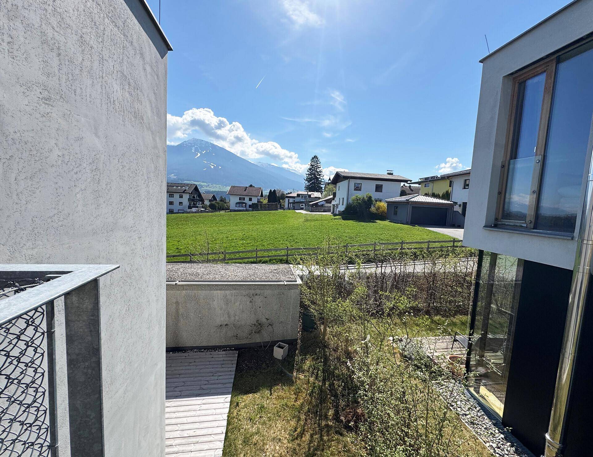 Weitläufiger Blick von einem Balkon auf grüne Felder und die majestätischen Berge.