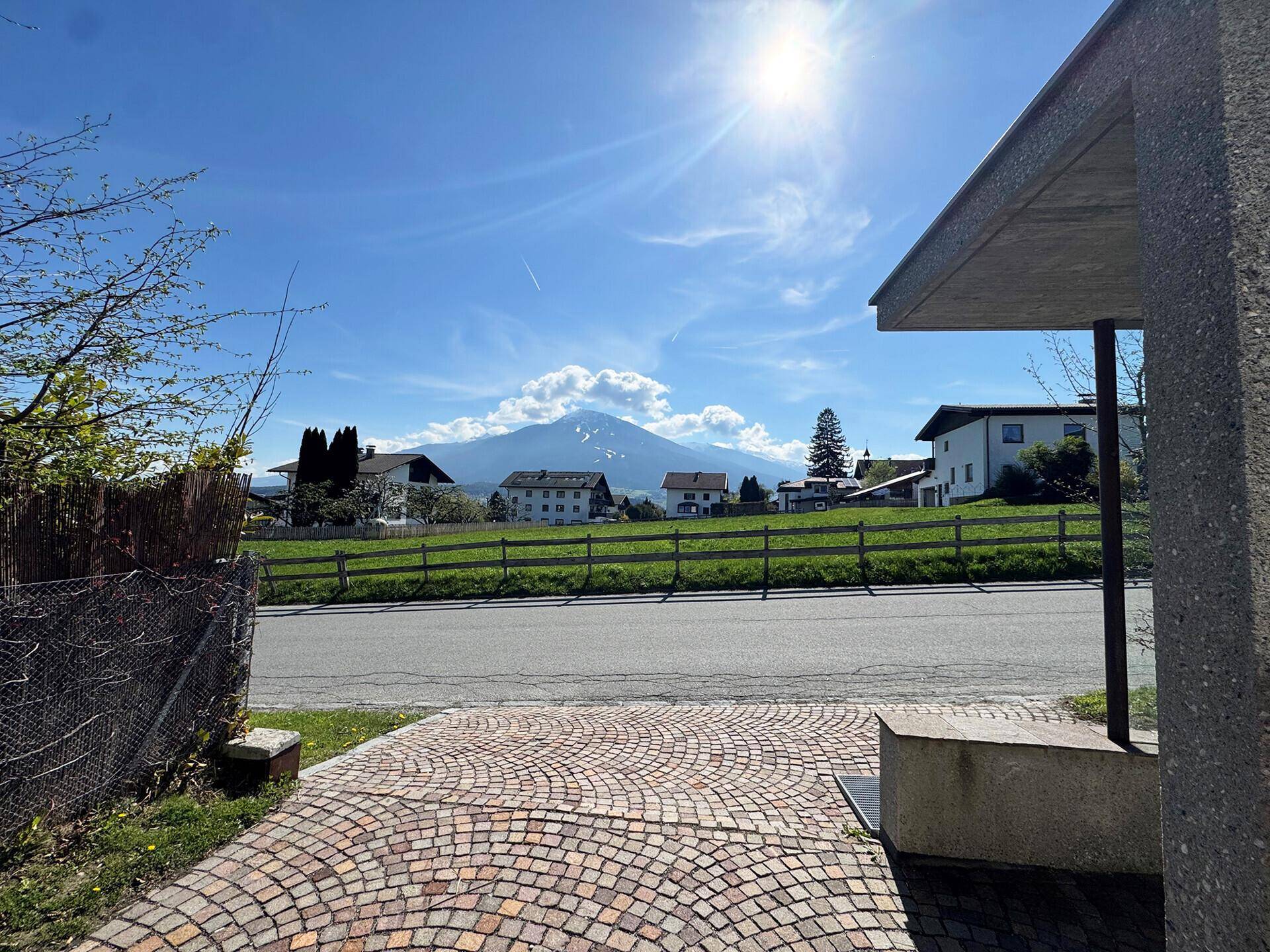 Sonnige Ansicht der Umgebung mit grünen Feldern, Bergen und der gepflasterten Zufahrt.