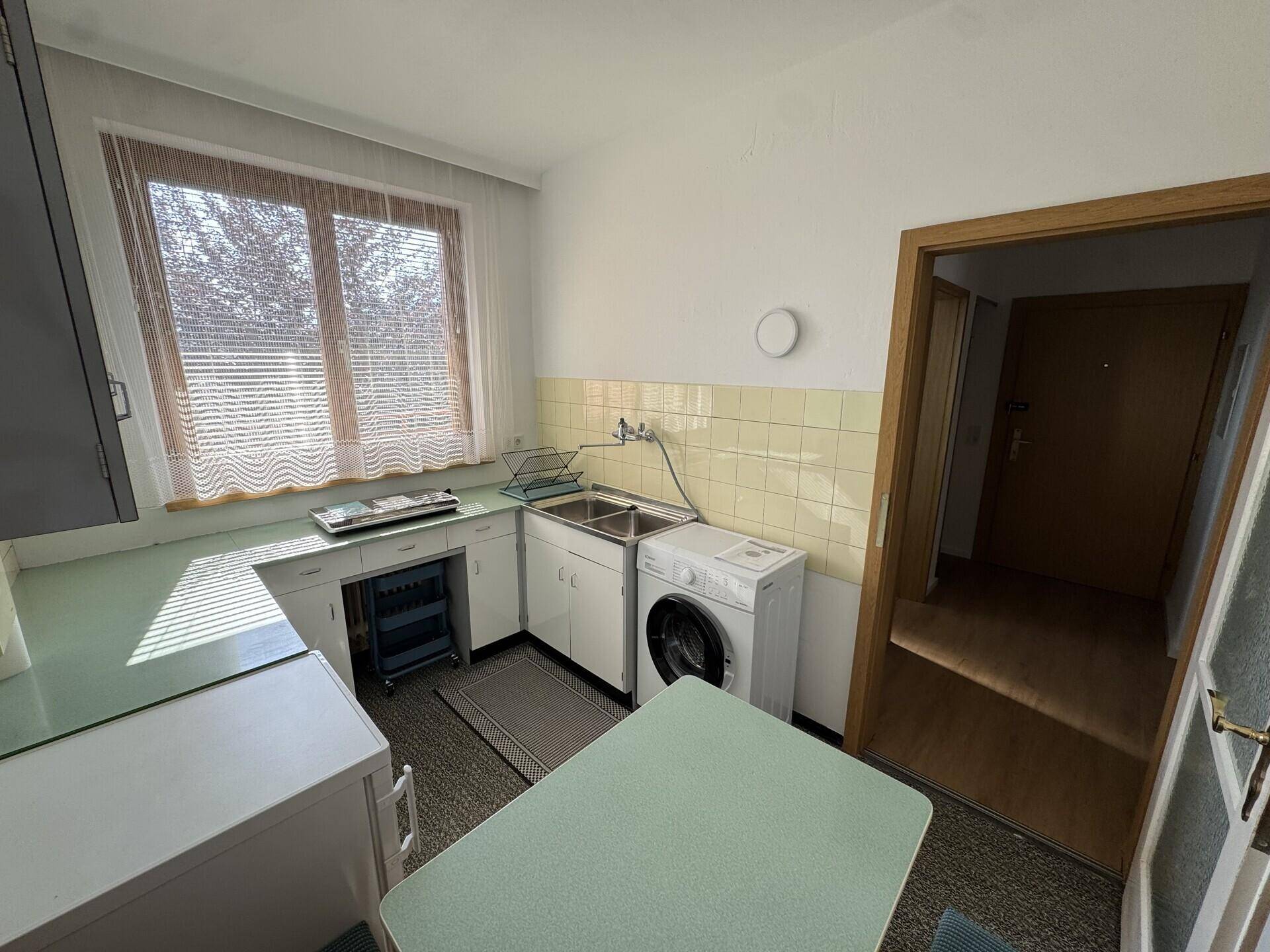 Helle Küche mit Spülbecken, Waschmaschine und Fenster, bietet ausreichend Arbeitsfläche und Stauraum.