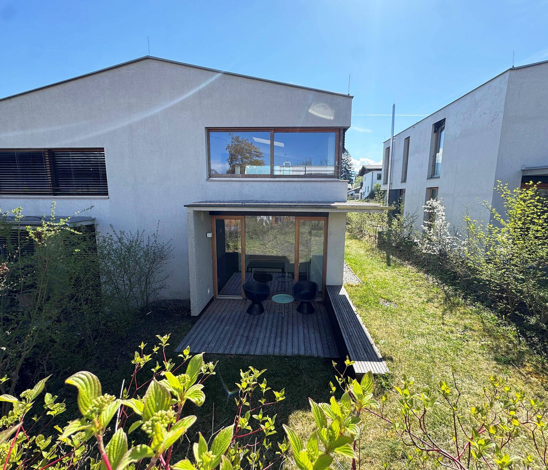 Rückseite des Hauses mit Holzterrasse, Garten und Blick auf die umliegende Bebauung.