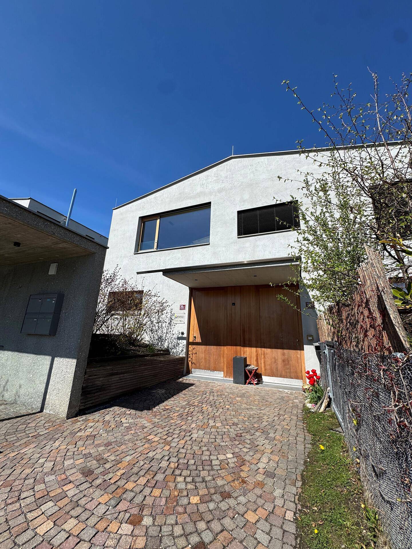 Moderne Hausfassade mit Holztor und gepflasterter Auffahrt unter blauem Himmel.