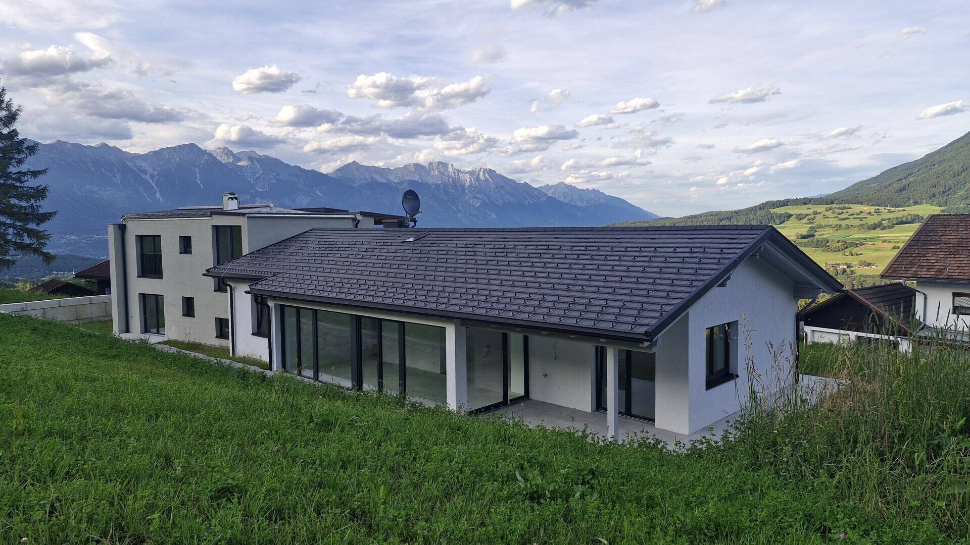 Modernes Wohnhaus in alpiner Landschaft mit großen Fensterfronten und Blick auf die Berge.