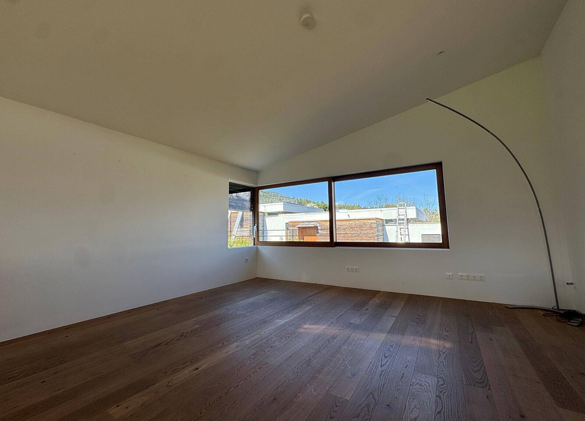 Heller, leerer Raum mit Holzboden und großen Fenstern, die viel Tageslicht hereinlassen.