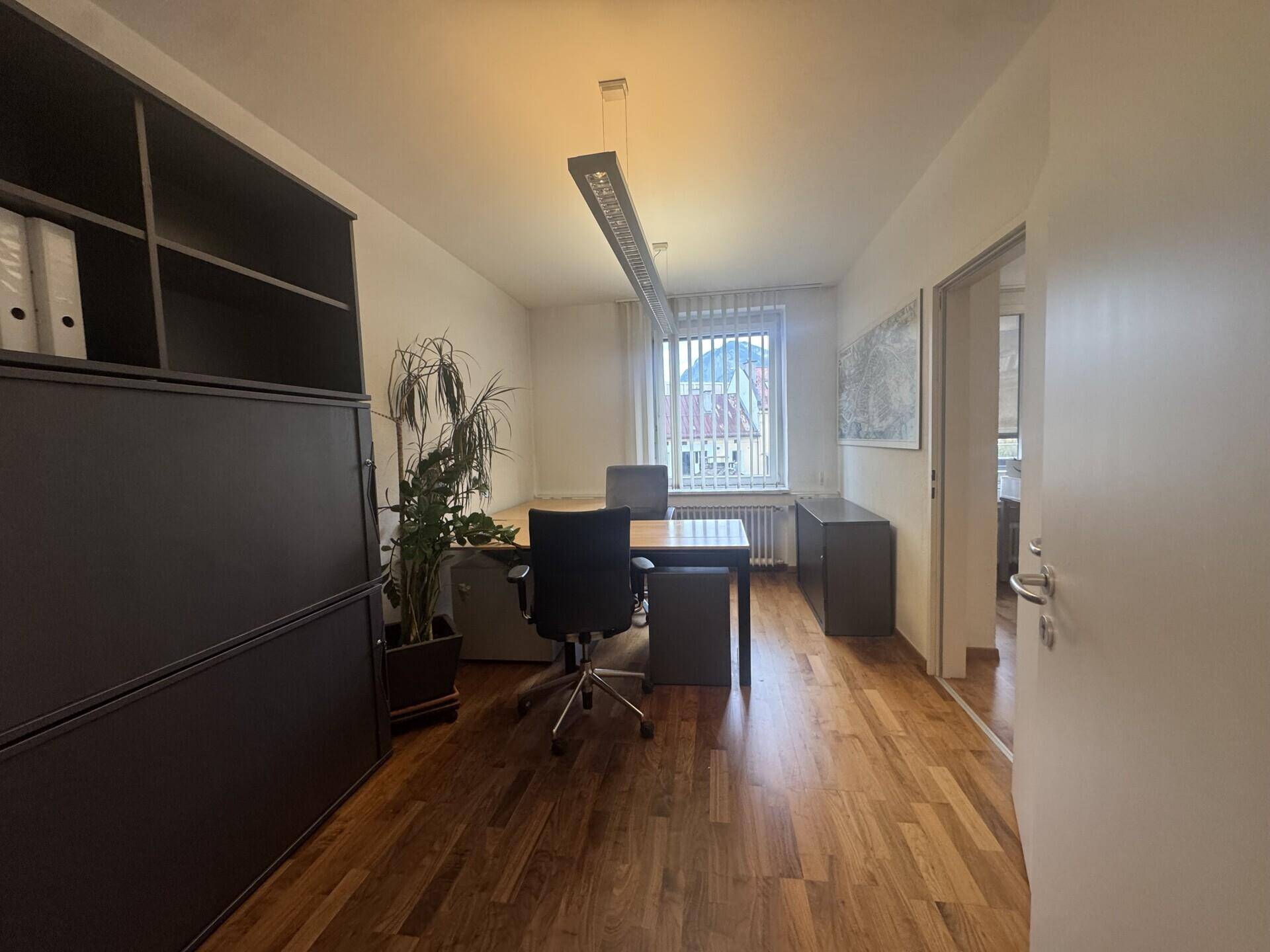 Langes Büro mit Holzboden, Schreibtisch, Bürostuhl und einem großen Regal, das viel Stauraum bietet.