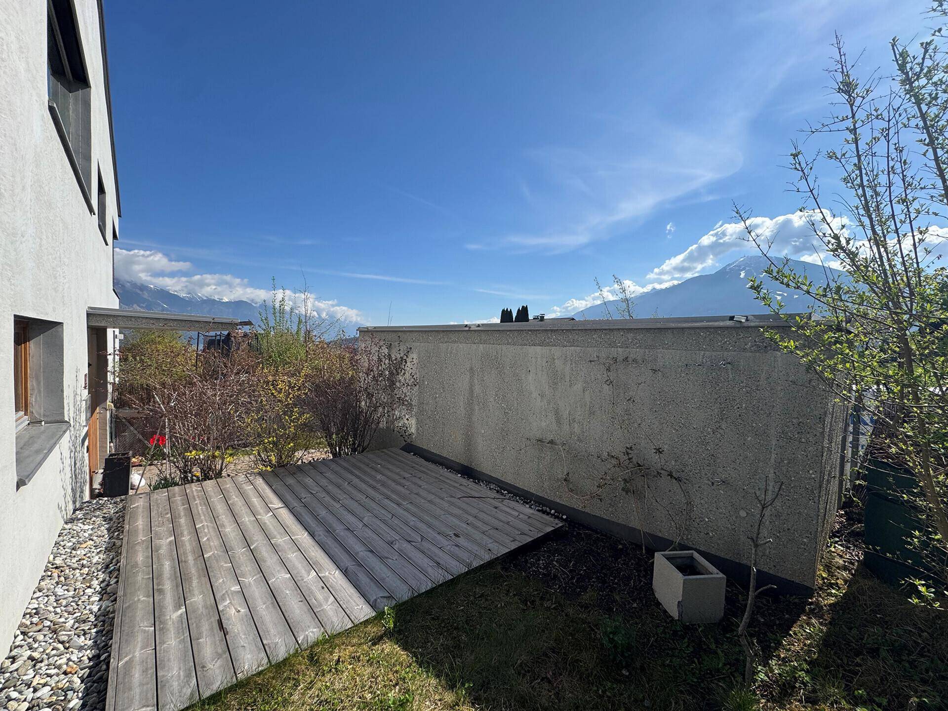 Holzterrasse im Gartenbereich mit Blick auf die ferne Bergkette und den blauen Himmel.