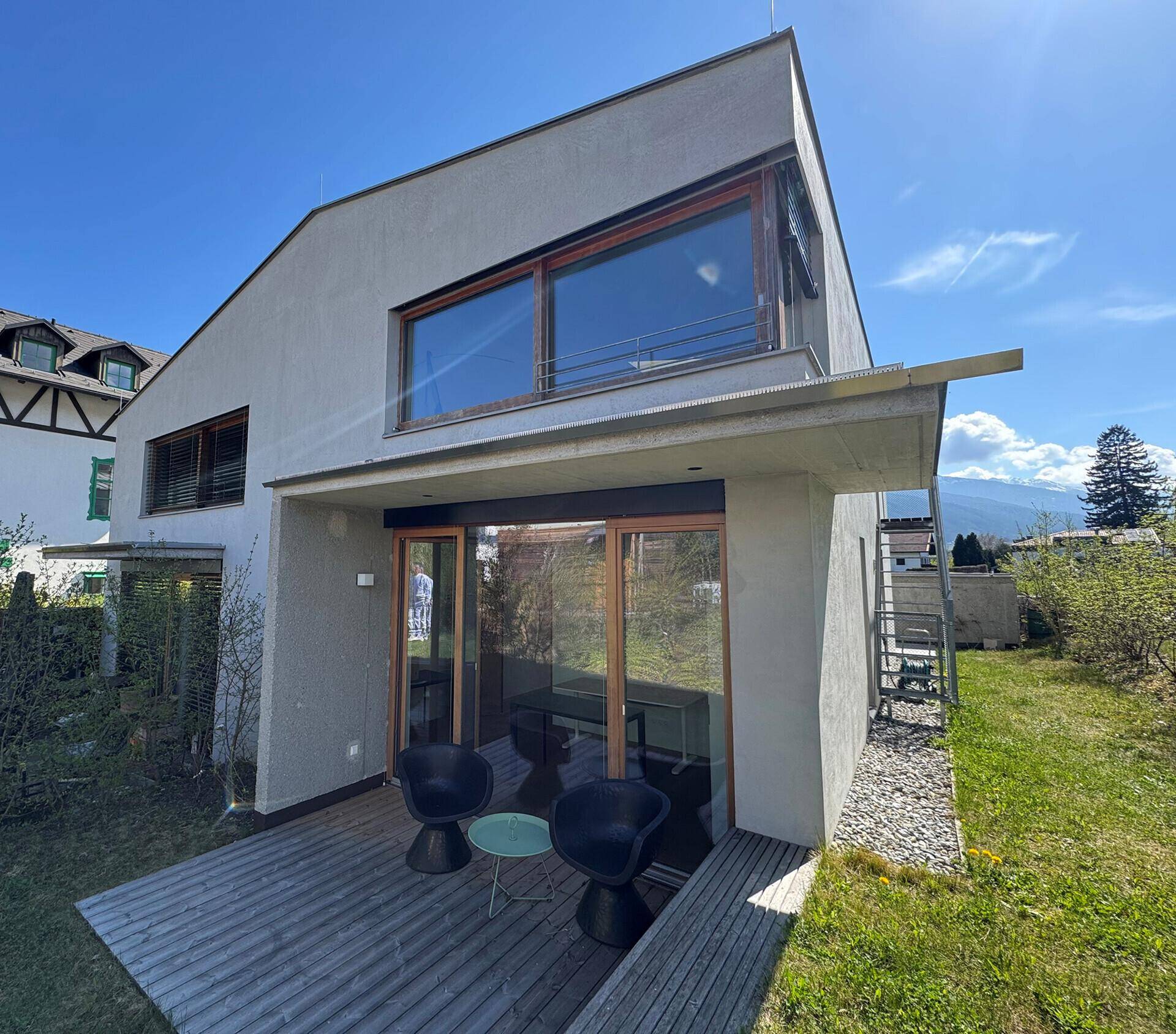 Rückseite des Hauses mit Holzterrasse, Garten und Blick auf die Berge in der Ferne.