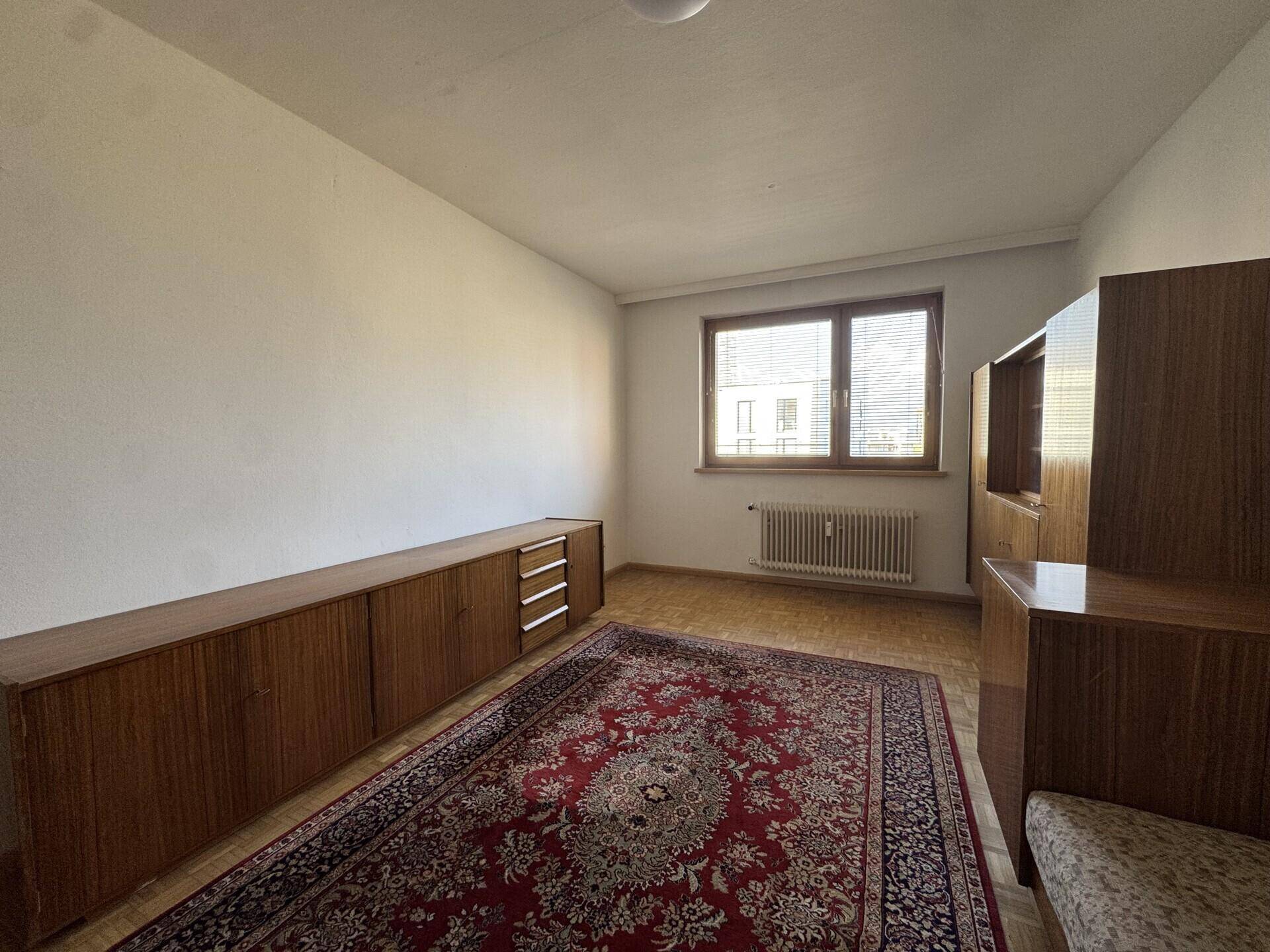Geräumiges Wohnzimmer mit Holzmöbeln und einem großen Teppich, bietet viel Platz und eine warme Atmosphäre.