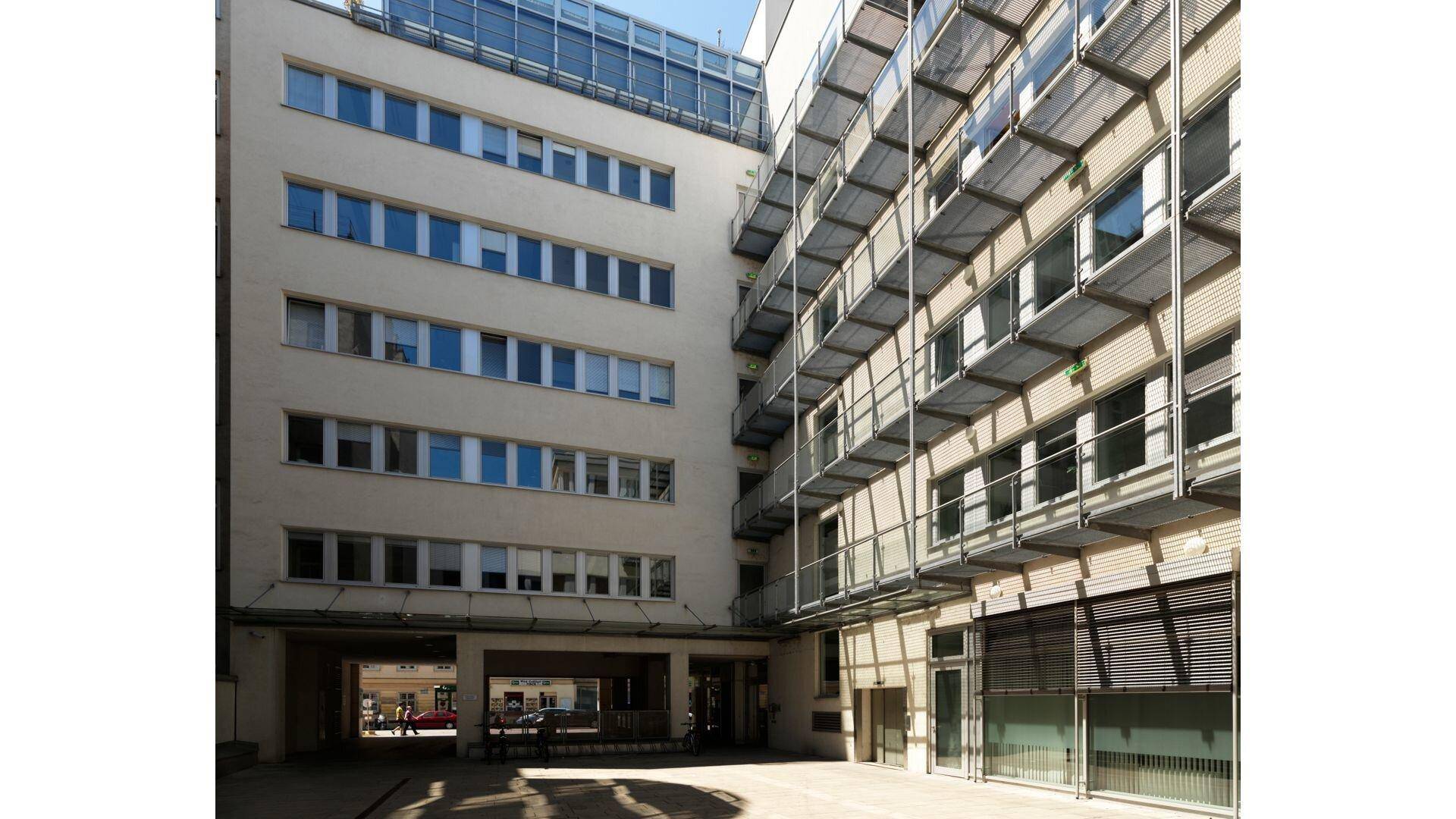 Blick in einen hellen Innenhof zwischen zwei Gebäudeteilen mit mehreren Etagen und Balkonen.