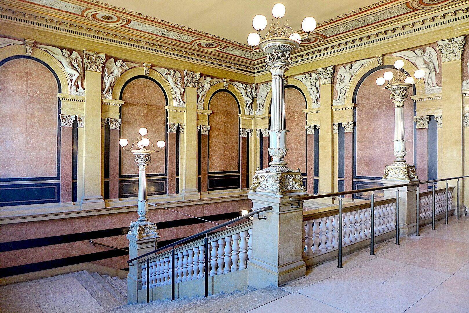 Prunkvolles Treppenhaus mit aufwendigen Stuckarbeiten, Säulen und Marmorverkleidungen in einem historischen Gebäude.