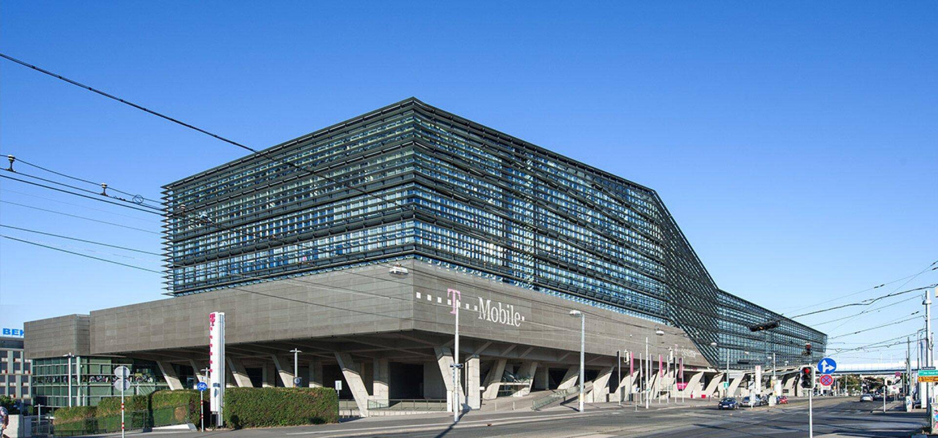 Großes, modernes Bürogebäude mit Glasfassade und T-Mobile-Logo an der Seite, umgeben von einer Straße.