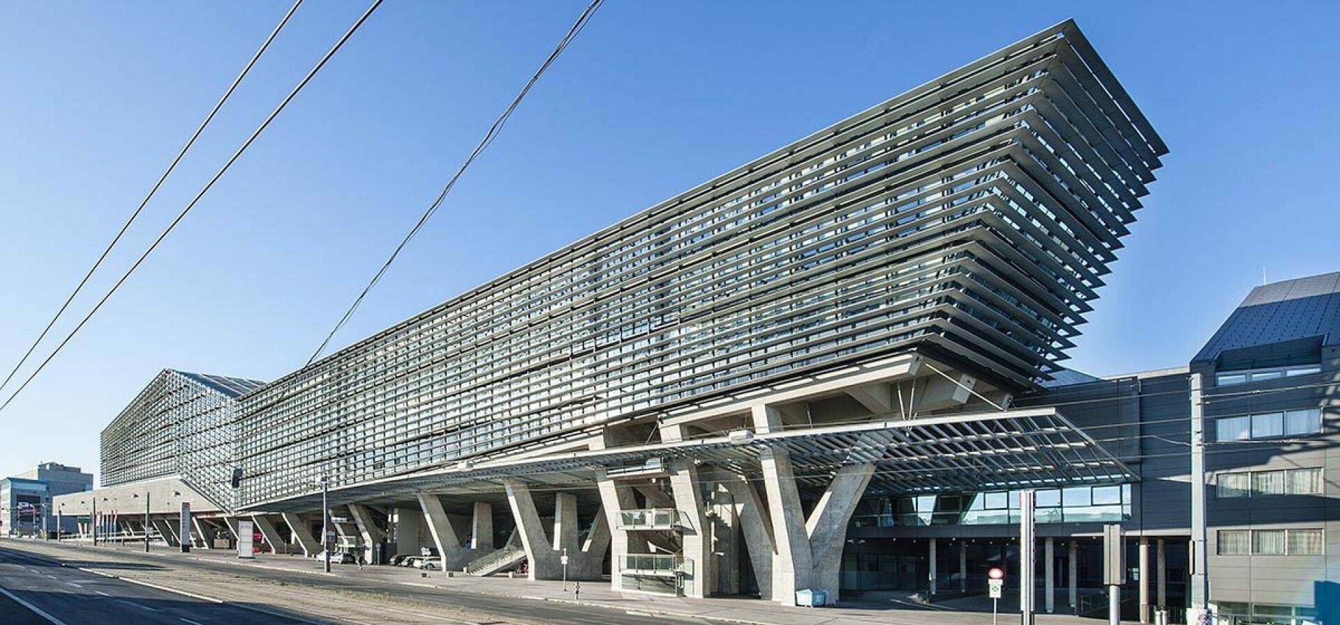 Moderne Architektur mit markanter Glasfassade und horizontalen Lamellen, getragen von massiven Betonstützen.