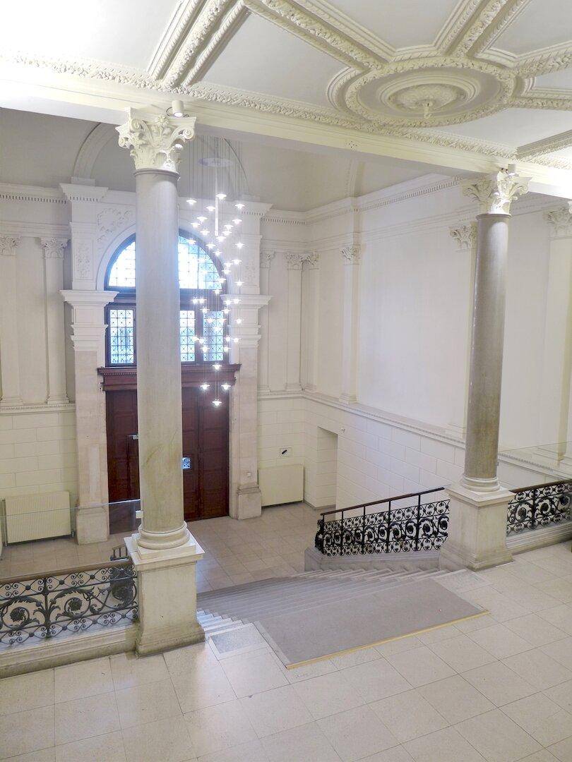 Repräsentativer Eingangsbereich mit hohen Decken, Säulen, Stuckverzierungen und einer eleganten Treppe.
