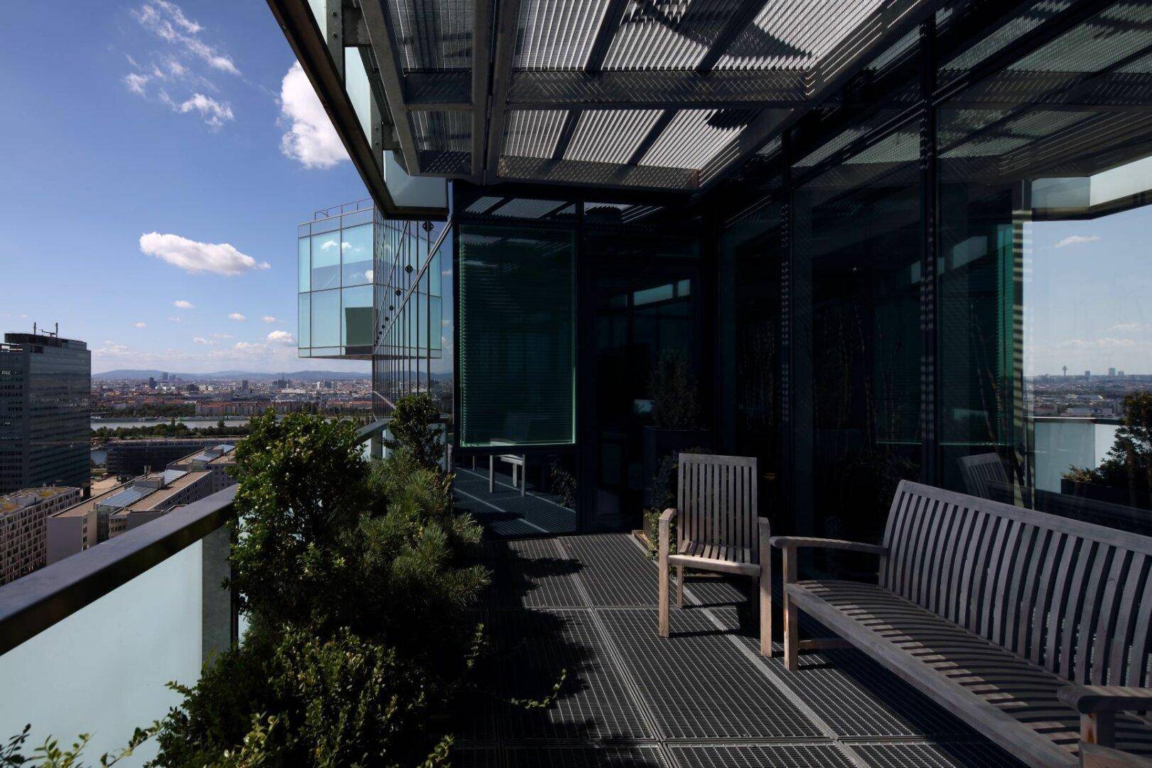 Großer Balkon mit Holzbänken und einem weiten Blick über die Stadt und die umliegende Landschaft.