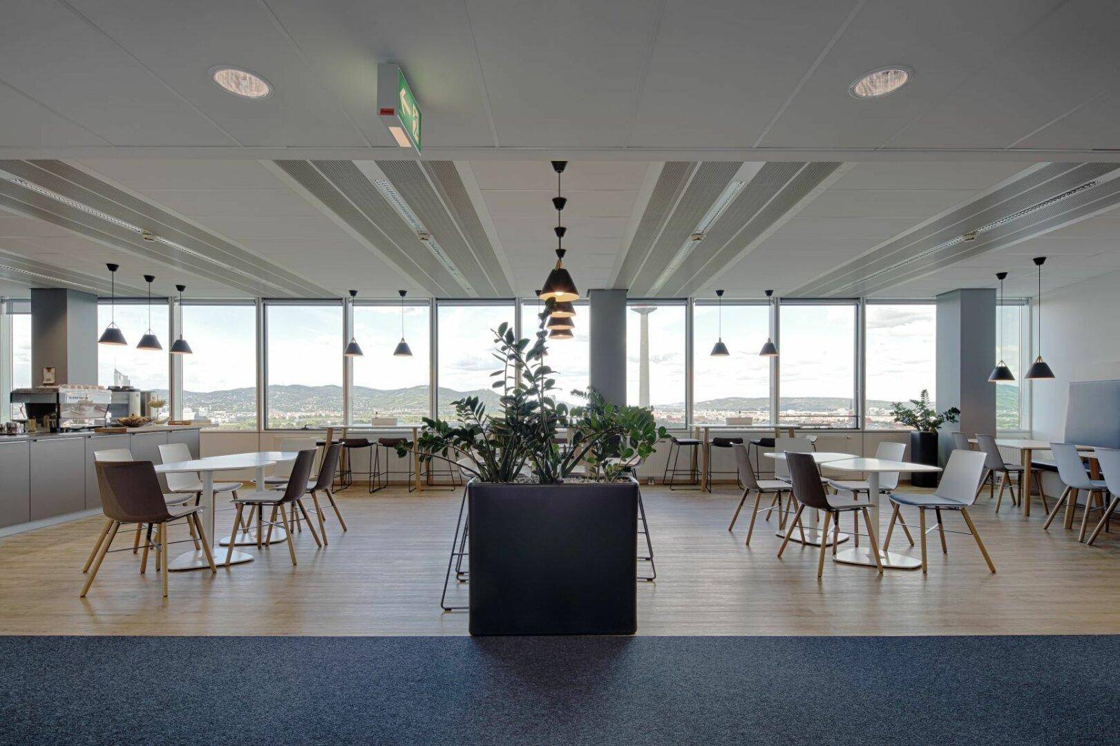 Geräumige Cafeteria mit Holzboden, großen Fenstern und verschiedenen Sitzgelegenheiten mit Stadtblick.