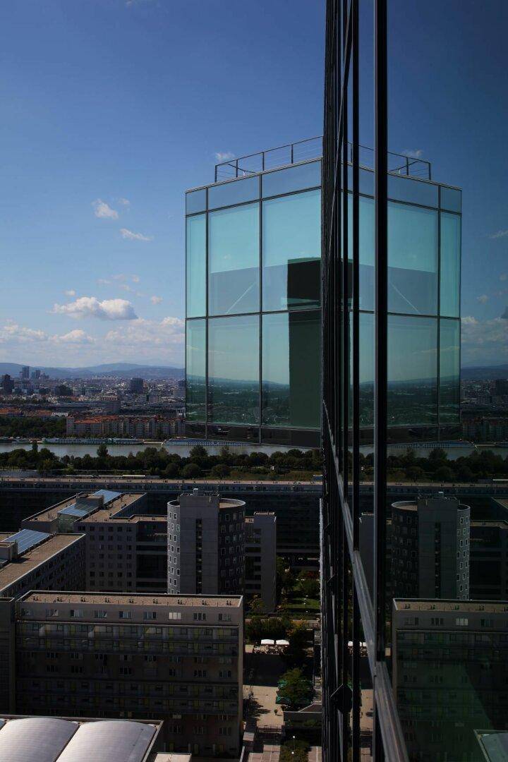 Moderne Glasfassade eines Hochhauses spiegelt die umliegende Stadtlandschaft und den Himmel wider.