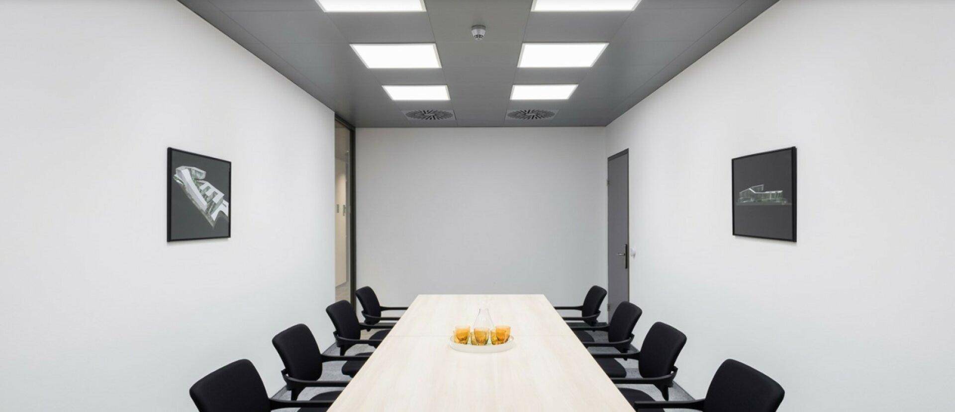 Heller Konferenzraum mit langem Tisch, schwarzen Stühlen und minimalistischer Dekoration an den Wänden.
