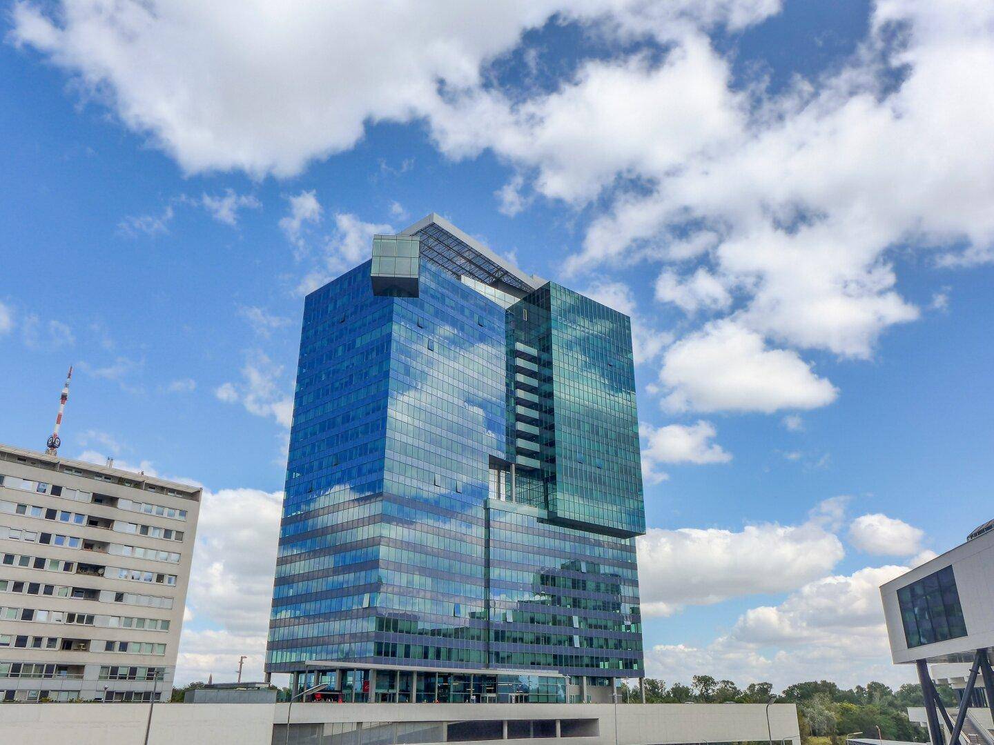 Modernes Hochhaus mit spiegelnder Glasfassade unter einem blauen Himmel mit weißen Wolken.