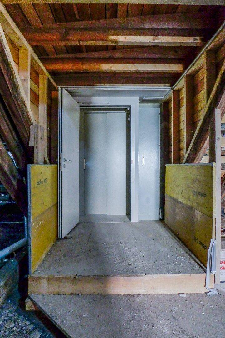 Aufzug im Rohbau des Dachgeschosses, umgeben von Holzkonstruktionen und Bauelementen.